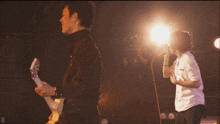 a man playing a guitar next to another man singing into a microphone with the letter d on the bottom right