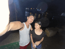a man and a woman are posing for a picture in front of a body of water
