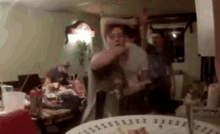 a group of people dancing in a living room with a plate of food in the foreground