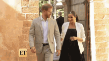 a man in a suit and a woman in a black dress are walking in front of a brick building .
