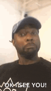 a man wearing a hat and a black shirt is making a funny face and saying `` ok , see you ! ''