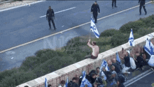 a man is sitting on a wall holding a flag in front of a group of people