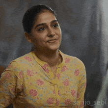 a woman in a yellow and pink floral shirt is smiling and looking down