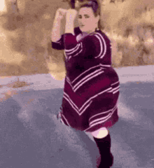 a woman in a purple and white dress is dancing on the street .
