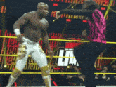 a man in a pink shirt is standing in a wrestling ring next to a man in a white and gold outfit
