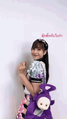 a girl is holding a purple teletubbies doll on her back