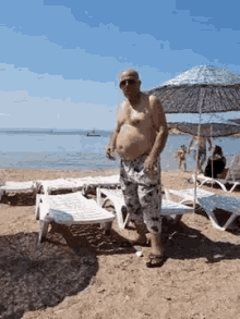 a shirtless man standing on a beach with umbrellas and lounge chairs