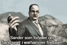 a man in a suit and tie is standing in front of a mountain holding a gun .