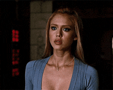 a woman wearing a blue sweater and a necklace looks at the camera