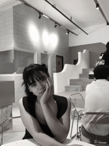 a black and white photo of a woman sitting at a table with her hand on her chin