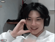 a young man wearing headphones is smiling and making a heart with his hands