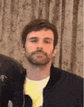 a close up of a man with a beard wearing a black jacket and a yellow t-shirt .
