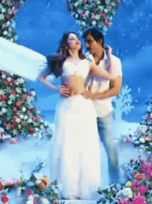 a man is holding a woman in a white dress in front of flowers