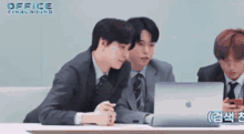a group of men in suits and ties are sitting at a table with a laptop .