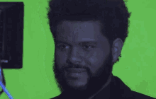 a man with a beard and curly hair is standing in front of a green screen .