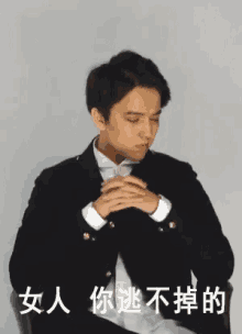 a man in a suit is sitting in a chair with his hands folded in front of him .