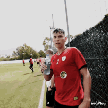 a man in a red jersey with the number 2 on it holds a bottle of water