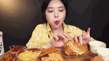 a woman is sitting at a table eating fried chicken and a hamburger
