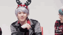a man with purple hair is wearing a reindeer headband and a studded jacket .
