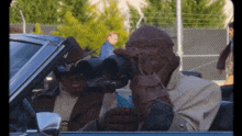 a man in a car looking through binoculars with a cup in his hand