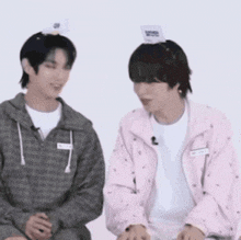 two young men are sitting next to each other and one of them is wearing a pink jacket .