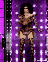 a drag queen is standing on a stage in front of a purple curtain with lights behind her .