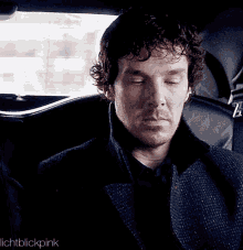 a man is sitting in the back seat of a car with his eyes closed and a beard .