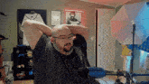 a bald man with glasses and a beard is sitting in front of a microphone with his hands behind his head