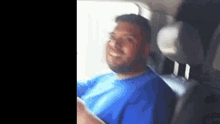a man in a blue shirt is sitting in a car and smiling .