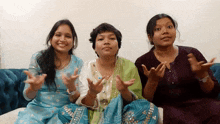 three women sitting on a couch with their hands up