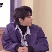 a man in a purple jacket is sitting at a table with his arms crossed .