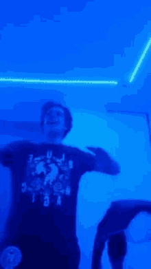 a man in a black shirt is dancing in a dark room with blue lights .
