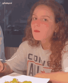 a girl wearing a converse shirt is sitting at a table