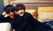 two young men are laying on a couch and one of them is smiling .