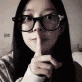 a woman wearing glasses has her finger to her mouth