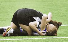 two female soccer players laying on the field with one wearing a black jersey with the letter a on it