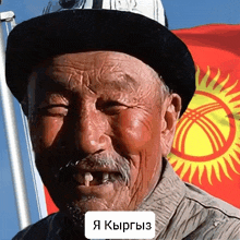 a man wearing a black hat is smiling in front of a flag with a sun on it