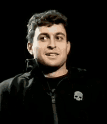a man wearing a black jacket with a skull on the back is smiling .