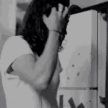 a woman is standing in front of a refrigerator and covering her face with her hands .