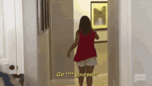 a woman in a red top and white shorts is walking down a hallway and says `` go yourself '' .