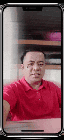 a man in a red shirt takes a selfie on a cell phone