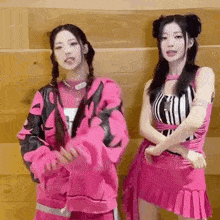 two girls in pink clothes are standing next to each other on a wooden wall .