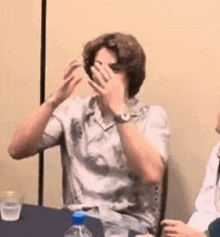 a man is sitting at a table with his hands on his face .