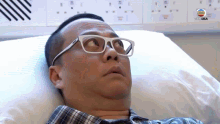a man wearing glasses is laying in a hospital bed looking up .