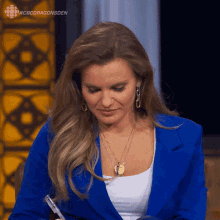a woman in a blue jacket is sitting in front of a cbs dragonsden sign