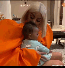 a woman in an orange dress is holding a baby in her arms