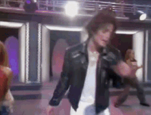 a man in a leather jacket is singing into a microphone on stage .