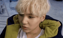 a close up of a person 's face with blonde hair and a green jacket