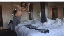a shirtless man is jumping on a bed with white sheets