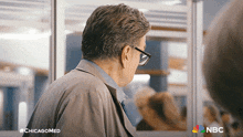 a man wearing glasses stands in front of a nbc ad
